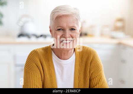 Porträt einer glücklichen älteren Dame, die in der Küche sitzt Stockfoto