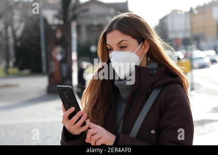 Portrait der Frau trägt Winterjacke mit FFP2 KN95 Maske Mit dem Smartphone im Freien Stockfoto