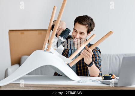 Mann, der Möbel fixiert, Holzstuhl repariert, mit Elektrobohrer zu Hause Stockfoto