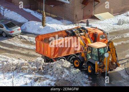 Winterschnee Entfernung von Gehwegen. Ein Mini-Traktor schaufelt Schnee und lädt ihn in die Rückseite eines LKW. Blick von oben. Stockfoto