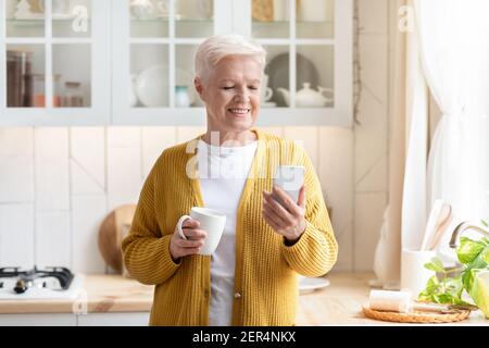 Moderne alte Dame mit Handy beim Tee trinken Stockfoto