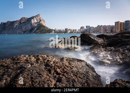 Blick von den Felsen der Küste mit dem städtischen Strand von Calpe und der Klippe im Hintergrund, Alicante, Spanien Stockfoto