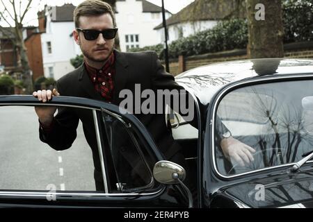 Junger Mann, der aus Auto vintage schwarz volkswagen Käfer Stockfoto