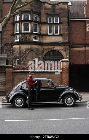 Junger Mann, der aus Auto vintage schwarz volkswagen Käfer Stockfoto