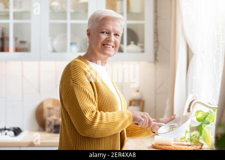 Fröhliche ältere Frau, die in der Küche Geschirr abspülte Stockfoto