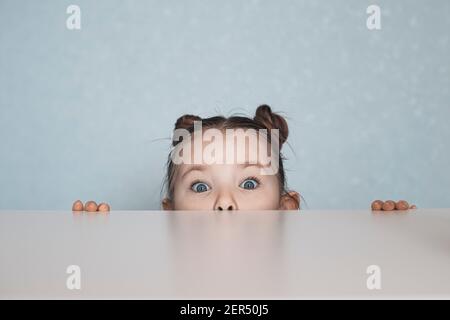 Portrait des kleinen Mädchens, das unter dem Tisch schaut. Hochwertige Fotos Stockfoto