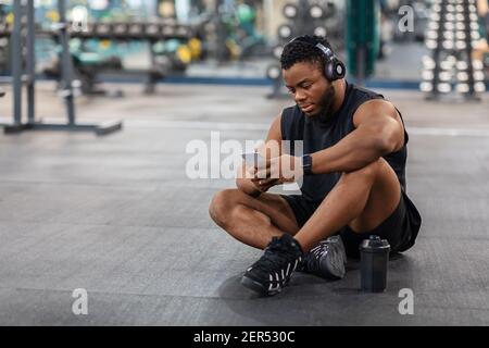 Müde schwarzen Kerl Bodybuilder sitzen auf dem Boden, Musik hören Stockfoto