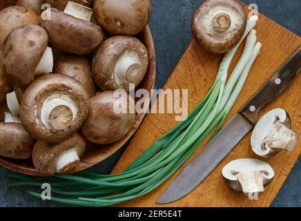 Champignon-Pilze in einer Holzschüssel und grüne Zwiebeln, Nahaufnahme, Draufsicht, geringe Schärfentiefe Stockfoto