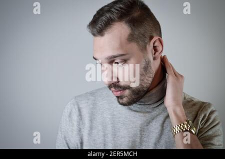 Porträt eines jungen Mannes mit einem kurzen Bart, dass Sieht verlegen im Gespräch und berührt seinen Hals Stockfoto