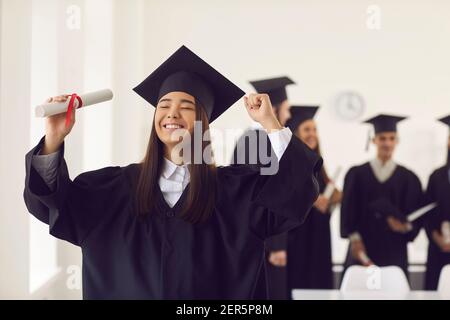 Porträt einer jungen Studentin, die mit geschlossenen Augen glücklich ist und ein Diplom hält. Stockfoto