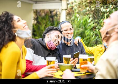 Multirassische Menschen lächeln mit offener Gesichtsmaske im Garten Des Restaurants beim Biertrinken - Neues normales Lifestyle-Konzept Über glückliche Freunde havi Stockfoto