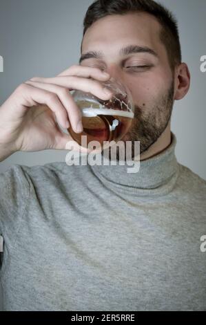 Porträt eines jungen Mannes mit einem kurzen Bart, der Trinkt ein Glas Bier Stockfoto