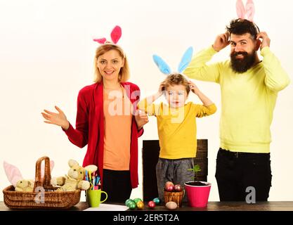 Glückliche Familie sitzen auf Holztisch mit Ostereiern. Kind hält Korb mit bemalten Eiern. Stockfoto