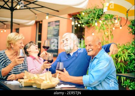 Ältere Leute lachen und rösten Rotwein im Restaurant - Freundschaftskonzept mit glücklichen reifen Freunden, die Spaß zusammen haben Zuhause im Garten Stockfoto