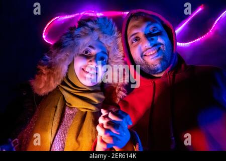 Happy arabisch muslimische Geschwister mit farbigen Lichtern hinter ihnen in Dunkles Zimmer Stockfoto