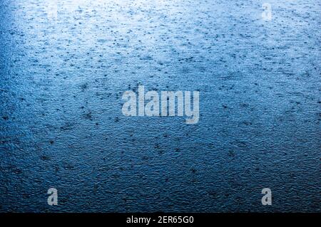 Blaue Hintergrundbilder von Regentropfen fallen in einen Körper von Wasser Stockfoto