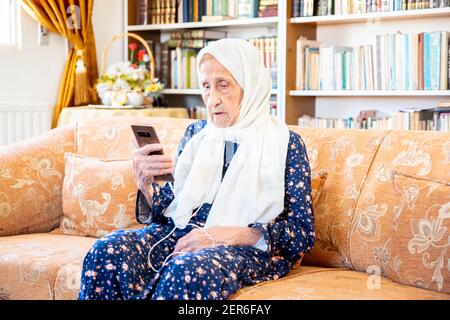 Happy arabisch muslim alte Frau trägt Kopfhörer zu hören Musik von ihrem Smartphone Stockfoto