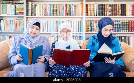 Glückliche muslimische Großmutter und Mutter und Enkelin sitzen zusammen Sofa liest Bücher Stockfoto