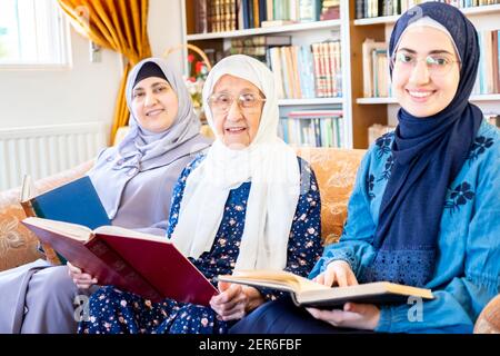 Glückliche muslimische Großmutter und Mutter und Enkelin sitzen zusammen Sofa liest Bücher Stockfoto