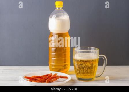 Bier aus einer Plastikflasche in einen Glaskrug gegossen Und Scheiben getrockneten Fischs auf einem Teller Stockfoto