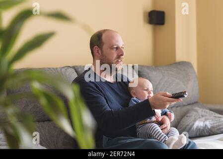 Das häusliche Leben des Vaters in Vaterschaftsurlaub. Vater und Sohn Fußball im Fernsehen zu Hause. Zu Hause in Zeiten der Pandemie Stockfoto