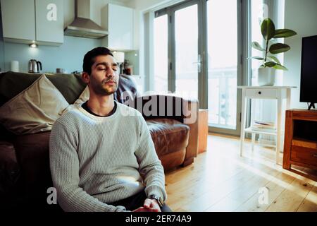 Gemischter Geschäftsmann, der in der Lounge auf dem Boden sitzt Meditieren vor der Arbeit Stockfoto