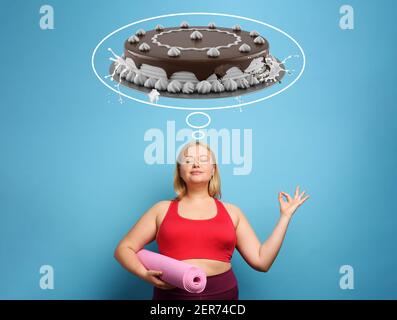 Fat Mädchen tut Fitness-Studio zu Hause, aber sie denkt immer über Süßigkeiten. Cyanfarbener Hintergrund Stockfoto