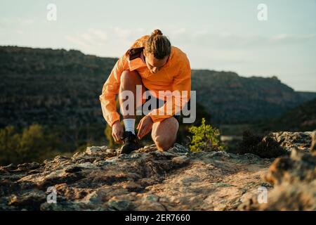 Kaukasischen männlichen Athleten eine Pause Binden Schuh Spitze während Rennen in der Wildnis Berg bei Sonnenuntergang Stockfoto