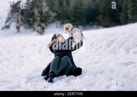 Junge Frau spielt mit einem pommerschen Hund auf dem Schnee Stockfoto