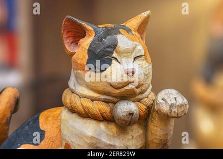 tokio, japan - februar 28 2021: Nahaufnahme einer Holzskulptur, die das Gesicht einer niedlichen japanischen Maneki-Neko-Katze mit einer Pfote zeigt, die in einer winkenden Form angehoben wurde Stockfoto