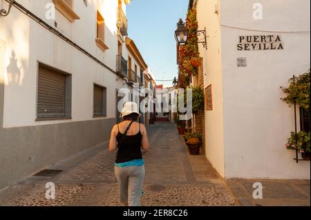Sevilla, Spanien 07-12-2010: Eine junge kaukasische Frau trägt ärmellose Bluse, Seitentasche ein breiter Rand raffia Eimer Hut läuft allein in einer engen alle Stockfoto