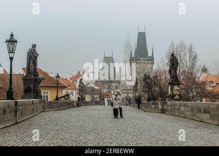 Prag, Tschechische Republik - 24. Februar 2021.Frauen mit Gesichtsmaske gegen covid19 Coronavirus zu Fuß auf nebligen Karlsbrücke.Erwachsene mit OP-Maske Stockfoto