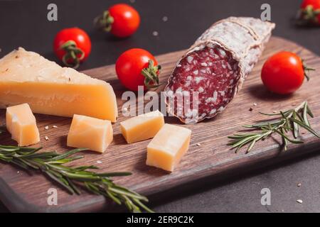 Geräucherte Schinkenwurst und geschnittene Scheiben mit Rosmarin und Kirsche Tomaten auf dunklem Holzbrett Stockfoto