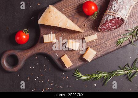 Geräucherte Schinkenwurst und geschnittene Scheiben mit Rosmarin und Kirsche Tomaten auf dunklem Holzbrett Stockfoto