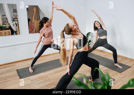 Flexible Frauen üben Yoga vor dem Lehrer, halten Krieger Pose Stockfoto