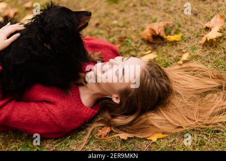 Frau umarmt Hund im Sommer Park. Fröhliche Dame mit langen dunklen Haaren Umarmungen und Striche freundlich alten Hund sitzt auf üppig grünen Wiese der öffentlichen Garde Stockfoto