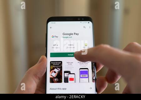 Ein Mann, der die Google Pay App auf einem Smartphone installiert, indem er mit dem Finger die Schaltfläche Installieren wählt. Google Pay ist eine digitale Wallet-Plattform Stockfoto