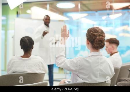 Rückansicht bei jungen Menschen, die Hände heben, während sie einem medizinischen Seminar im College zuhören, Platz kopieren Stockfoto