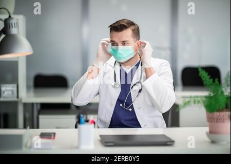 Ein junger Therapeut in einer medizinischen Maske sitzt in seinem Büro in einer Privatklinik Stockfoto