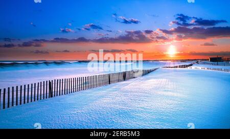 Winterszene unter farbigem Himmel bei Sonnenuntergang am schneebedeckten Strand. Jones Beach State Park, Long Island NY Stockfoto