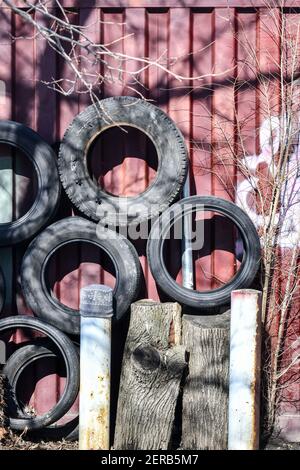 Gestapelte und verlassene gebrauchte Gummireifen gegen rot verwittertes Holz Wand Stockfoto