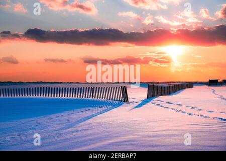 Winterszene unter farbigem Himmel bei Sonnenuntergang am schneebedeckten Strand. Jones Beach State Park, Long Island NY Stockfoto