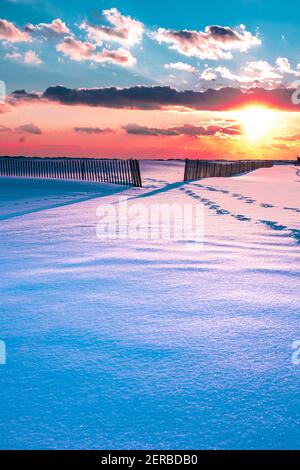 Winterszene unter farbigem Himmel bei Sonnenuntergang am schneebedeckten Strand. Jones Beach State Park, Long Island NY Stockfoto