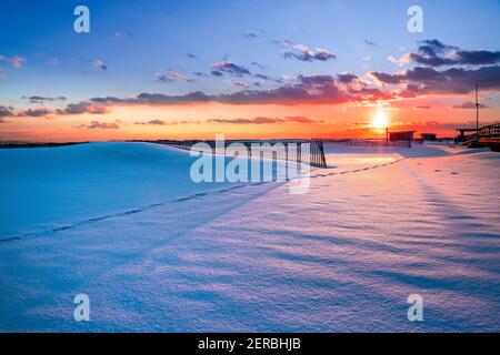 Winterszene unter farbigem Himmel bei Sonnenuntergang am schneebedeckten Strand. Jones Beach State Park, Long Island NY Stockfoto