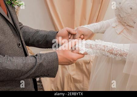 Die Hände des männlichen Bräutigams halten die Hände der Braut in Hochzeitshandschuhen. Stockfoto