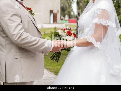 Die Braut und der Bräutigam halten die Hände bei einem Hochzeitsspaziergang aus nächster Nähe. Stockfoto