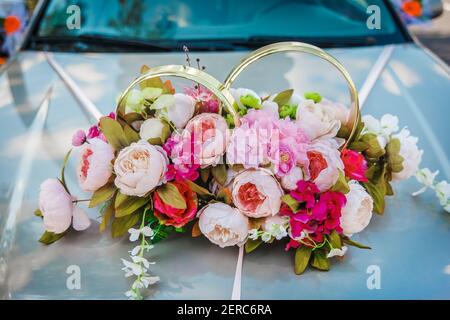 Dekoration von künstlichen Blumen von Rosen und Eheringe auf der Haube des Autos close-up. Stockfoto