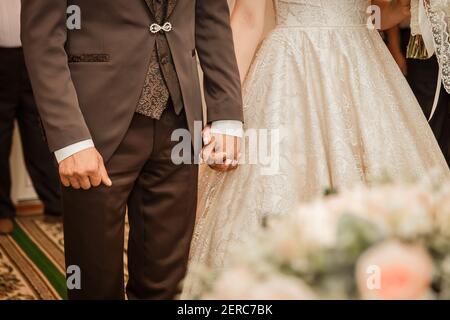 Der Bräutigam in einem braunen Anzug hält die Hand der Braut fest. Stockfoto