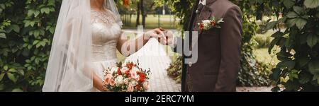 Der Bräutigam im braunen Anzug hält die Hand der Braut mit einem Hochzeitsstrauß. Stockfoto