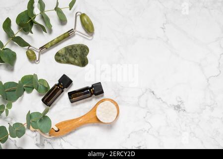 Natürliche Hautpflege-, Spa- und Wellness-Tools: Beauty Jade Roller, Sha Sha Stein, ätherisches Öl und Holzpinsel mit Eukalyptuszweig auf Marmor Bac Stockfoto